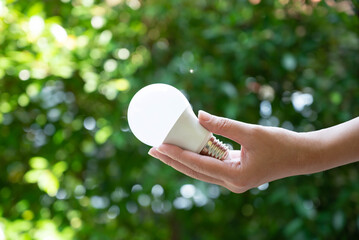 LED bulb in woman hand with green grass background for ecology concept