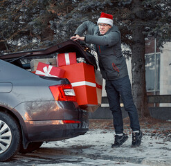 Man trying to close the trunk of a car filled with boxes after shopping. Too many purchases are too much. A full trunk of holiday packages and boxes with gifts.  © Anton