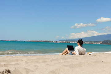 Young woman using laptop computer on a beach. Vacation lifestyle communication. Freelance work concept