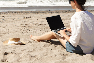 Young woman using laptop computer on a beach. Vacation lifestyle communication. Freelance work concept