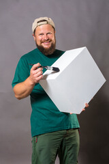 Joyful bearded foreman in green t-shirt with brush and blanc object looks like cube