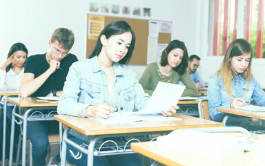 positive adult schoolgirl is sitting test and answer about task in the classroom.
