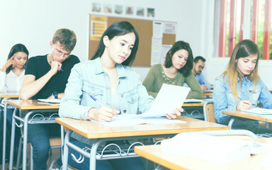 Fototapeta premium positive adult schoolgirl is sitting test and answer about task in the classroom.