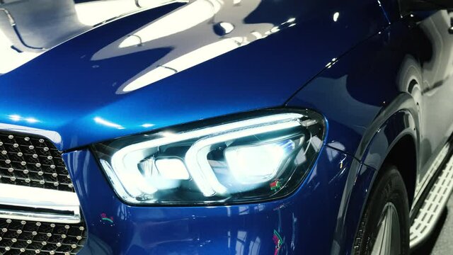 Turns on and off the dipped and main beam headlights. Close-up of the headlight of a new blue car in the showroom. Modern laser headlights. Led lights. Xenon. Bixenon.