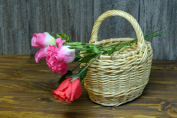 Fototapeta na wymiar Artificial flowers in a wicker basket on a wooden background