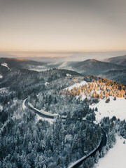 Aerial View of a scenic Highway passing in the Carpathian Mountain Landscape during a colorful winter sunrise. 