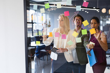 Diverse business people brainstorming by glass board in office