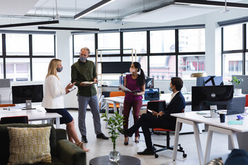 Diverse business people wearing face masks brainstorming in office