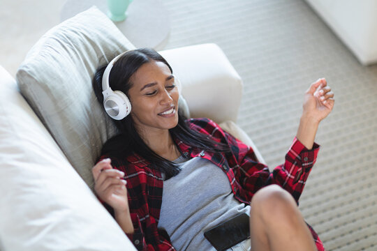 Mixed race woman lying on couch with headphones listening to music at home