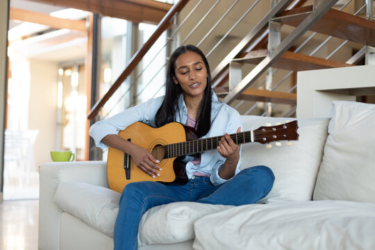 Mixed race woman sitting on couch playing guitar at home