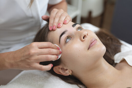 Caucasian woman lying back while beautician wipes her eyebrows