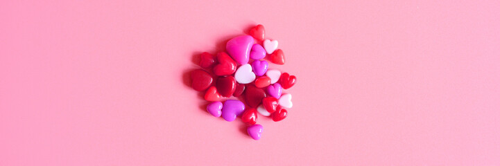a heap of heart shaped glossy beads in different pink shades on a pink background. banner. space for text