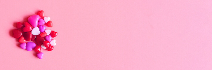 a heap of heart shaped glossy beads in different pink shades on a pink background. banner. space for text