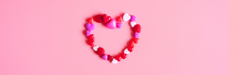 a heap of heart form glossy beads in different pink shades laid out in the shape of a heart on a pink background. banner