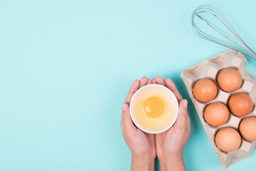 Fresh egg in a bowl holding by woman hand preparing for cooking on color background, Top view