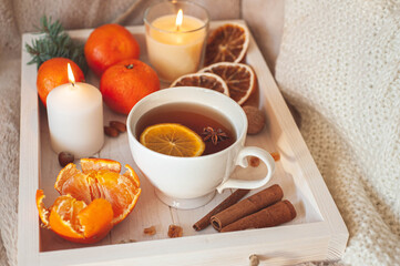 Obraz na płótnie Canvas A wooden tray with tea, tangerines, nuts and spices on a beige plaid. Winter breakfast. The concept of hygge.