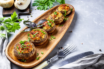  Baked stuffed mushrooms on a wooden plate and gray background, top view, copy space