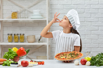 child making tasty delicious gesture by kissing fingers. little girl in chef hat and an apron cooking pizza in the kitchen.