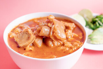 Exquisite Mexican Menudo on a white plate accompanied by a dish with condiments on the back.