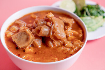Exquisite Mexican Menudo on a white plate accompanied by a dish with condiments on the back.