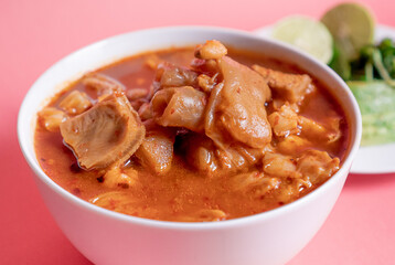 Exquisite Mexican Menudo on a white plate accompanied by a dish with condiments on the back.