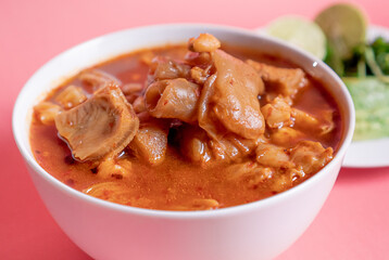 Exquisite Mexican Menudo on a white plate accompanied by a dish with condiments on the back.