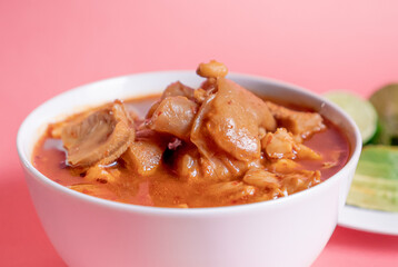 Exquisite Mexican Menudo on a white plate accompanied by a dish with condiments on the back.