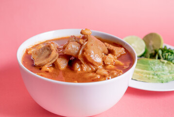 Exquisite Mexican Menudo on a white plate accompanied by a dish with condiments on the back.