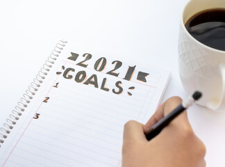 Decorated notebook for writing New Year's resolutions on a table with a coffee cup on the side and a hand writing.