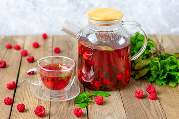 Herbal tea with berries, raspberries, mint leaves and hibiscus flowers in glass teapot and cup on wooden table Medicine for cold Vitamin drink Rustic style