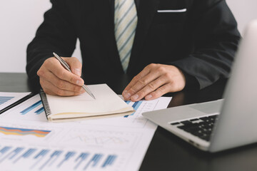 Businessmen or accountants sit, take notes or analyze data from graphs placed on their desks to assess risks and plan the future for the business.