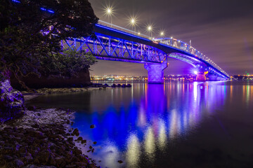 The Auckland Harbour Bridge, Auckland, New Zealand, with colorful nighttime lighting, reflected in...