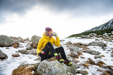 A woman traveler is resting with a metal mug of hot tea on a cold windy day.