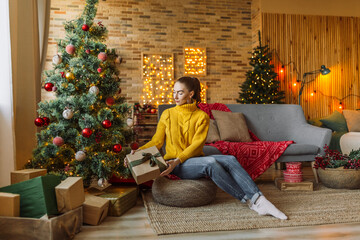 Obraz premium Beautiful cheerful happy young girl with christmas gifts on the background of a new year tree at home