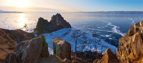  Beautiful frozen Lake Baikal at sunset. Panoramic view on the natural landmark of Olkhon Island - the famous Shamanka Rock or Burhan Cape and blue clear ice on the Small Sea Strait. Winter holidays