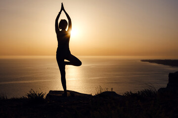 The woman with yoga posture on the mountain at sunset