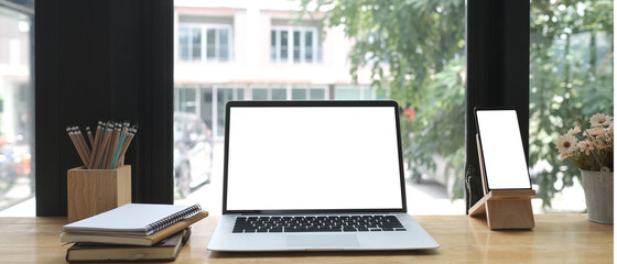 Fototapeta premium Front view of work place with laptop, smart phone and notebook on wooden table near window.