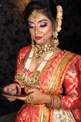 Portrait of very beautiful young Indian bride in luxurious bridal costume with makeup and heavy jewellery looking at mobile. Wedding fashion.