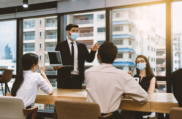 Office man wearing mask present and discuss work with team in meeting room. New normal office. Keep physical distancing.