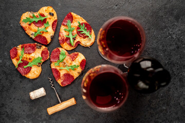 Dinner for two. Two heart shaped pepperoni pizzas and a bottle of red wine, glasses for Valentine's Day. Selective focus