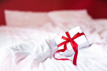 gift with a red ribbon in the shape of a heart for valentine's day lies on the bed of a hotel
