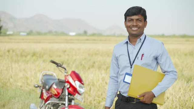Banker or corporate officer standing in front of motor bike and agriculture farmland - concept of Indian banker on field work and loan sanction.