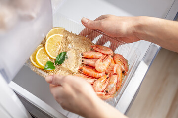 Women's hands are taking out a plastic container of rice, shrimps and lemon from the freezer of the fridge. Concept of ready made frozen dishes and saving time on cooking food