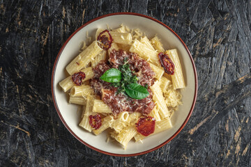 Plate of delicious appetizing vegetarian pasta with tomato sauce, tomatoes, cheese and basil on a black table. Top view