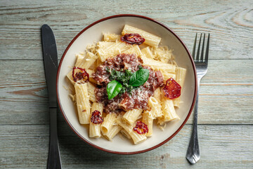 Plate of delicious appetizing vegetarian pasta with tomato sauce, tomatoes, cheese and basil on a wooden table. Top view