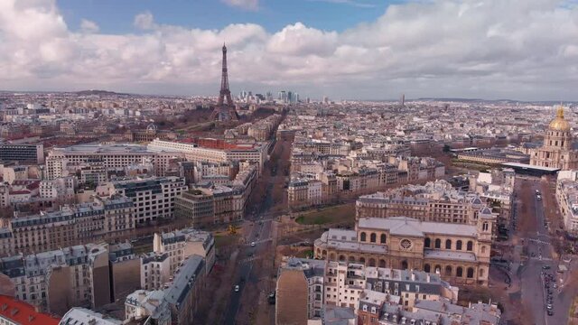 Aerial footage of Eiffel Tower. Camera descends showing Eiffel Tower, &Eacute;cole Militaire, Champ de Mars, the army museum and St Francis Xavier's Church in early spring blue sky covered with white clouds
