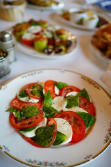 slicing tomatoes and mozzarella cheese with basil and spices on a plate.