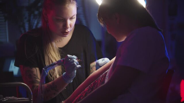 Young woman getting a tattoo by a woman master in dark studio