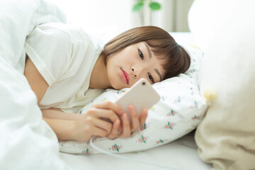 若い女性　ベッド　スマホ