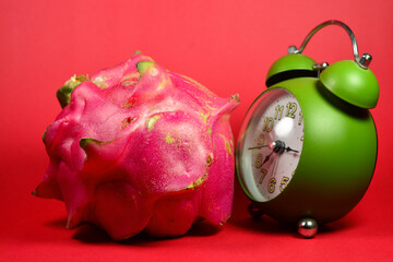 Whole fresh dragon fruit and alarm clock on red background. diet reminder photo illustration